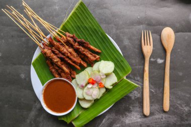 Tavuklu satay ya da satay tavuklu lontong, pirinç keki ve fıstık sosuyla servis edilir. Muz iznine ayrılmış.