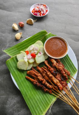 Tavuklu satay ya da satay tavuklu lontong, pirinç keki ve fıstık sosuyla servis edilir. Muz iznine ayrılmış.
