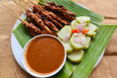 Tavuklu satay ya da satay tavuklu lontong, pirinç keki ve fıstık sosuyla servis edilir. Muz iznine ayrılmış.