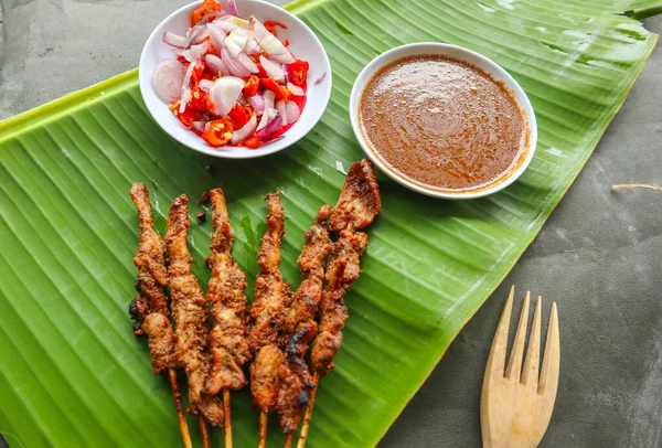 Tavuklu satay ya da satay tavuklu lontong, pirinç keki ve fıstık sosuyla servis edilir. Muz iznine ayrılmış.