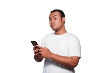 Beyaz tişört giyen heyecanlı Asyalı adam telefonunu tutarken gülümsüyor, beyaz arka planla izole edilmiş.