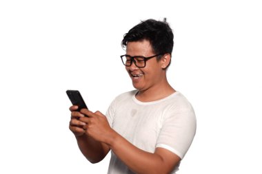 Gözlüklü, beyaz tişörtlü, tebessüm giymiş telefonuyla gülümseyen Asyalı heyecanlı bir adam.