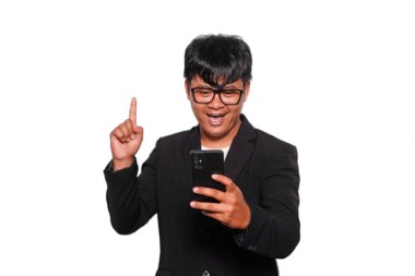 Gözlüklü, siyah takım elbiseli, tebessüm eden, beyaz arkaplan tarafından izole edilmiş telefonunu tutan heyecanlı Asyalı adam.