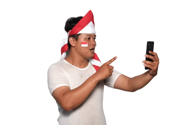 stock image Excited Asian man wearing white Tshirt smiling while holding his phone, isolated by white background. indonesian independence day celebration