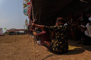 Klaten, Endonezya, 15 Ağustos 2023 Cava geleneklerine göre giyinmiş erkek ve kadın katılımcılar, geleneksel Cava ok ticaretinde hedef doğruluğu konusunda yoğunlaşmak için gözlerini kısarak selam verdiler.