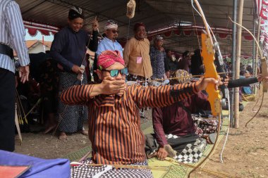 Klaten, Endonezya, 15 Ağustos 2023 Cava geleneklerine göre giyinmiş erkek ve kadın katılımcılar, geleneksel Cava ok ticaretinde hedef doğruluğu konusunda yoğunlaşmak için gözlerini kısarak selam verdiler.