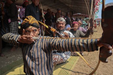 Klaten, Endonezya, 15 Ağustos 2023 Cava geleneklerine göre giyinmiş erkek ve kadın katılımcılar, geleneksel Cava ok ticaretinde hedef doğruluğu konusunda yoğunlaşmak için gözlerini kısarak selam verdiler.