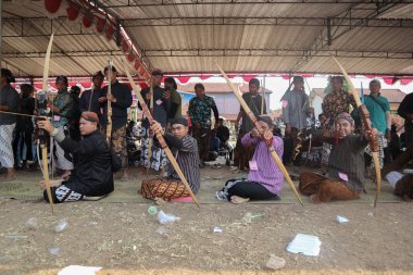 Klaten, Endonezya, 15 Ağustos 2023 Cava geleneklerine göre giyinmiş erkek ve kadın katılımcılar, geleneksel Cava ok ticaretinde hedef doğruluğu konusunda yoğunlaşmak için gözlerini kısarak selam verdiler.