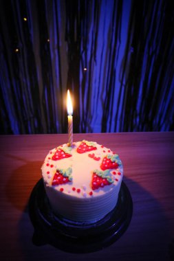 Çilekli doğum günü pastası ve mavi arka planda bir mum.