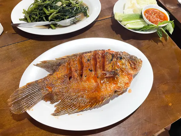 Izgara gourami veya Gurame bakar kırmızı barbekü sosu, sebze ve biber sosu ile masada yedili beyaz bir tabakta.