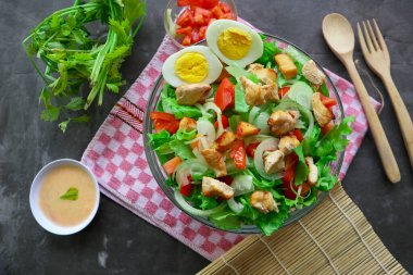 Marul, domates, yumurta ve tavukla dolu bir sezar salata kasesi. Salata şeffaf bir cam kasede servis edilir.
