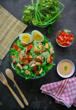 Marul, domates, yumurta ve tavukla dolu bir sezar salata kasesi. Salata şeffaf bir cam kasede servis edilir.