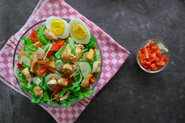 Marul, domates, yumurta ve tavukla dolu bir sezar salata kasesi. Salata şeffaf bir cam kasede servis edilir.