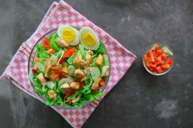 Marul, domates, yumurta ve tavukla dolu bir sezar salata kasesi. Salata şeffaf bir cam kasede servis edilir.