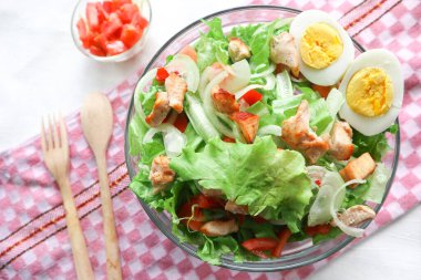 Marul, domates, yumurta ve tavukla dolu bir sezar salata kasesi. Salata şeffaf bir cam kasede servis edilir.