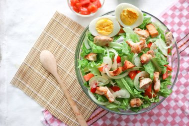 Marul, domates, yumurta ve tavukla dolu bir sezar salata kasesi. Salata şeffaf bir cam kasede servis edilir.