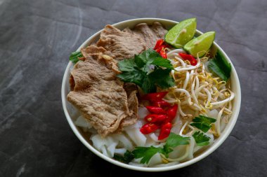 Biftek, pirinç eriştesi, zencefil, limon ve biberli geleneksel Pho Bo çorbası. Kapatın. Siyah arka planda servis edilen Vietnam mutfağı