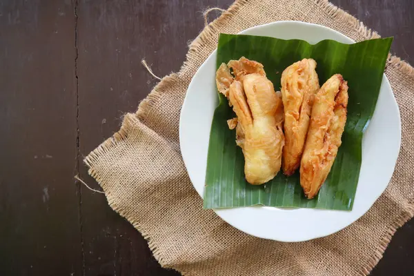 stock image fried bananas or pisang goreng served on a plate with banana leaf. The plate is on a wooden table