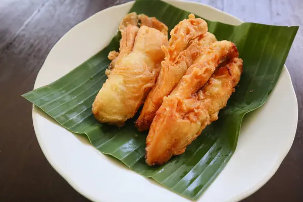 stock image fried bananas or pisang goreng served on a plate with banana leaf. The plate is on a wooden table