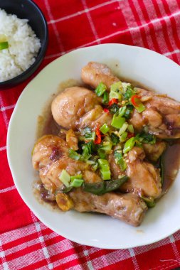 Üstünde yeşil sebzeler olan bir tabak tavuk. Tabak kırmızı bir bezin üzerinde. Tabak yemek dolu ve lezzetli görünüyor.