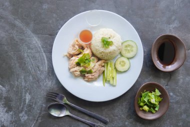 Salatalık dilimi, et suyu ve sos ile servis edilen tavuk çorbasıyla pişirilmiş tavuk pirinci veya nasi hainan veya pilav.