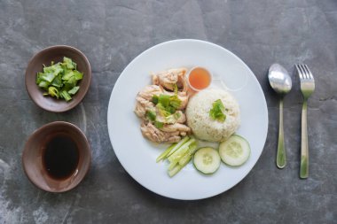 Salatalık dilimi, et suyu ve sos ile servis edilen tavuk çorbasıyla pişirilmiş tavuk pirinci veya nasi hainan veya pilav.