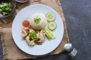 Salatalık dilimi, et suyu ve sos ile servis edilen tavuk çorbasıyla pişirilmiş tavuk pirinci veya nasi hainan veya pilav.