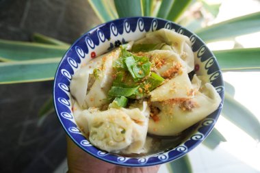 Bir kase wonton çorbası ve siyah arka planda servis edilen dilimlenmiş yeşil soğan.