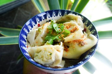 Bir kase wonton çorbası ve siyah arka planda servis edilen dilimlenmiş yeşil soğan.