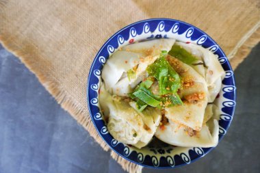 Bir kase wonton çorbası ve siyah arka planda servis edilen dilimlenmiş yeşil soğan.