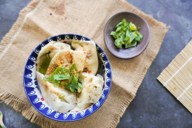 Bir kase wonton çorbası ve siyah arka planda servis edilen dilimlenmiş yeşil soğan.