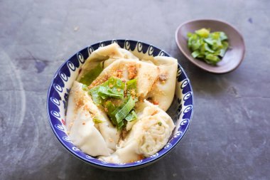 Bir kase wonton çorbası ve siyah arka planda servis edilen dilimlenmiş yeşil soğan.