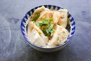 Bir kase wonton çorbası ve siyah arka planda servis edilen dilimlenmiş yeşil soğan.