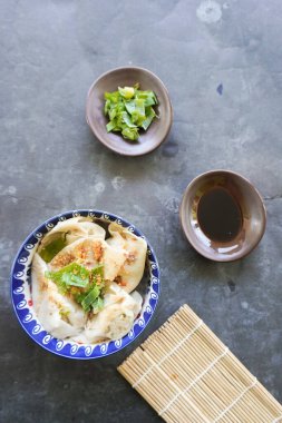 Bir kase wonton çorbası ve siyah arka planda servis edilen dilimlenmiş yeşil soğan.