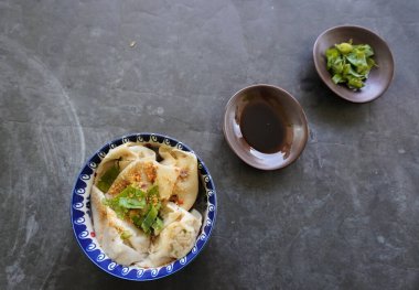 Bir kase wonton çorbası ve siyah arka planda servis edilen dilimlenmiş yeşil soğan.