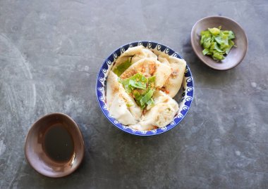 Bir kase wonton çorbası ve siyah arka planda servis edilen dilimlenmiş yeşil soğan.
