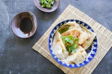 Bir kase wonton çorbası ve siyah arka planda servis edilen dilimlenmiş yeşil soğan.