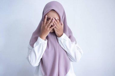 Mor tesettürlü genç Asyalı Müslüman kadın ağlıyor. Aşağı bakıyor ve elleri yüzünü kapatıyor.