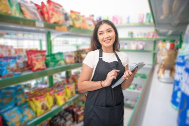 Gülümseyen Asyalı bir kadın market çalışanı olarak malzeme stoklarını kontrol ediyor.