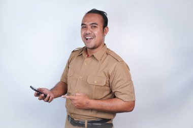 Asyalı bir devlet memuru ya da devlet memuru kahverengi üniformalı bir jest bandıyla telefonunu tutar ve fotokopi makinesini ona doğrultur. Beyaz arka planda. Endonezya PNS, ASN