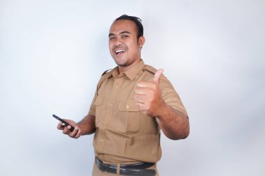 Asyalı bir devlet memuru ya da devlet memuru kahverengi üniformalı bir kafa bandıyla telefonunu tutar ve onaylar. Beyaz arka planda. Endonezya PNS, ASN