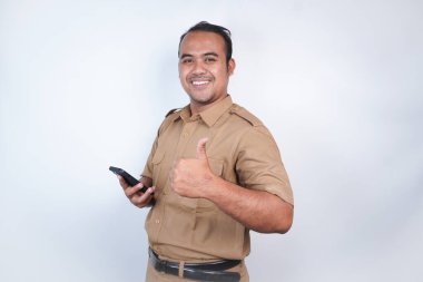 Asyalı devlet memurları veya devlet memurları gülümseyen bir adam kahverengi üniformalı bir jestle telefonunu gösterir. Beyaz arka planda. Endonezya PNS, ASN