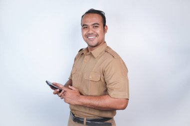 Asyalı devlet memurları veya devlet memurları gülümseyen bir adam kahverengi üniformalı bir jestle telefonunu gösterir. Beyaz arka planda. Endonezya PNS, ASN