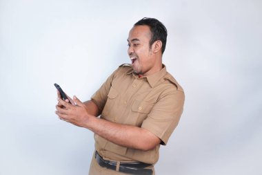 Asyalı devlet memurları veya devlet memurları gülümseyen bir adam kahverengi üniformalı bir jestle telefonunu gösterir. Beyaz arka planda. Endonezya PNS, ASN