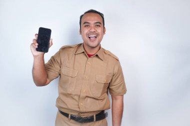 Asyalı devlet memurları veya devlet memurları gülümseyen bir adam kahverengi üniformalı bir jestle telefonunu gösterir. Beyaz arka planda. Endonezya PNS, ASN