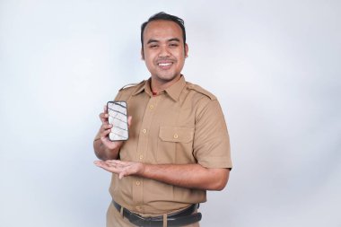 Asyalı devlet memurları veya devlet memurları gülümseyen bir adam kahverengi üniformalı bir jestle telefonunu gösterir. Beyaz arka planda. Endonezya PNS, ASN