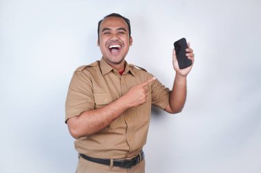 Asyalı devlet memurları veya devlet memurları gülümseyen bir adam kahverengi üniformalı bir jestle telefonunu gösterir. Beyaz arka planda. Endonezya PNS, ASN