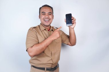 Asyalı devlet memurları veya devlet memurları gülümseyen bir adam kahverengi üniformalı bir jestle telefonunu gösterir. Beyaz arka planda. Endonezya PNS, ASN