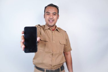Asyalı devlet memurları veya devlet memurları gülümseyen bir adam kahverengi üniformalı bir jestle telefonunu gösterir. Beyaz arka planda. Endonezya PNS, ASN