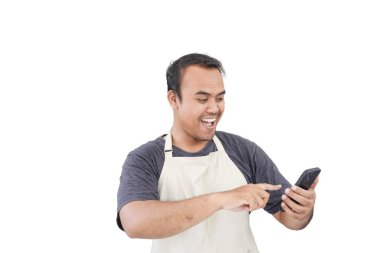 Asyalı erkek bakkal olarak çalışıyor ya da modern market çalışanları gülümsüyor, telefona mutlu bir şekilde bakıyor, izole beyaz arka planda dururken krem rengi önlük giyiyor.